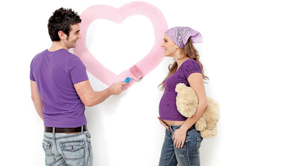 Young couple, husband and pregnant wife painting nursery wall.