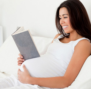 Good looking pregnant woman reading a book while lying on a bed