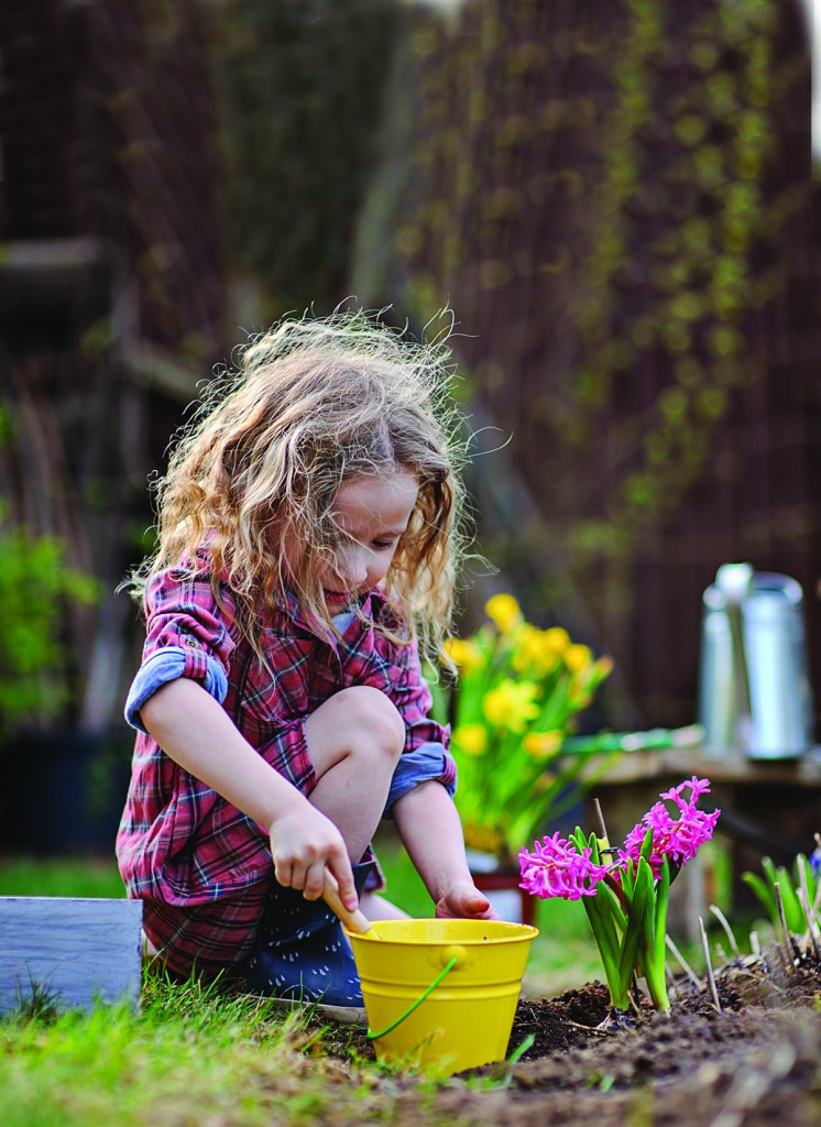 child girl planting flowers in spring garden