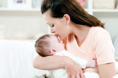 Young mother kissng her small sleeping newborn baby - indoors