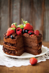Piece of chocolate cake with icing and fresh berry on wooden background
